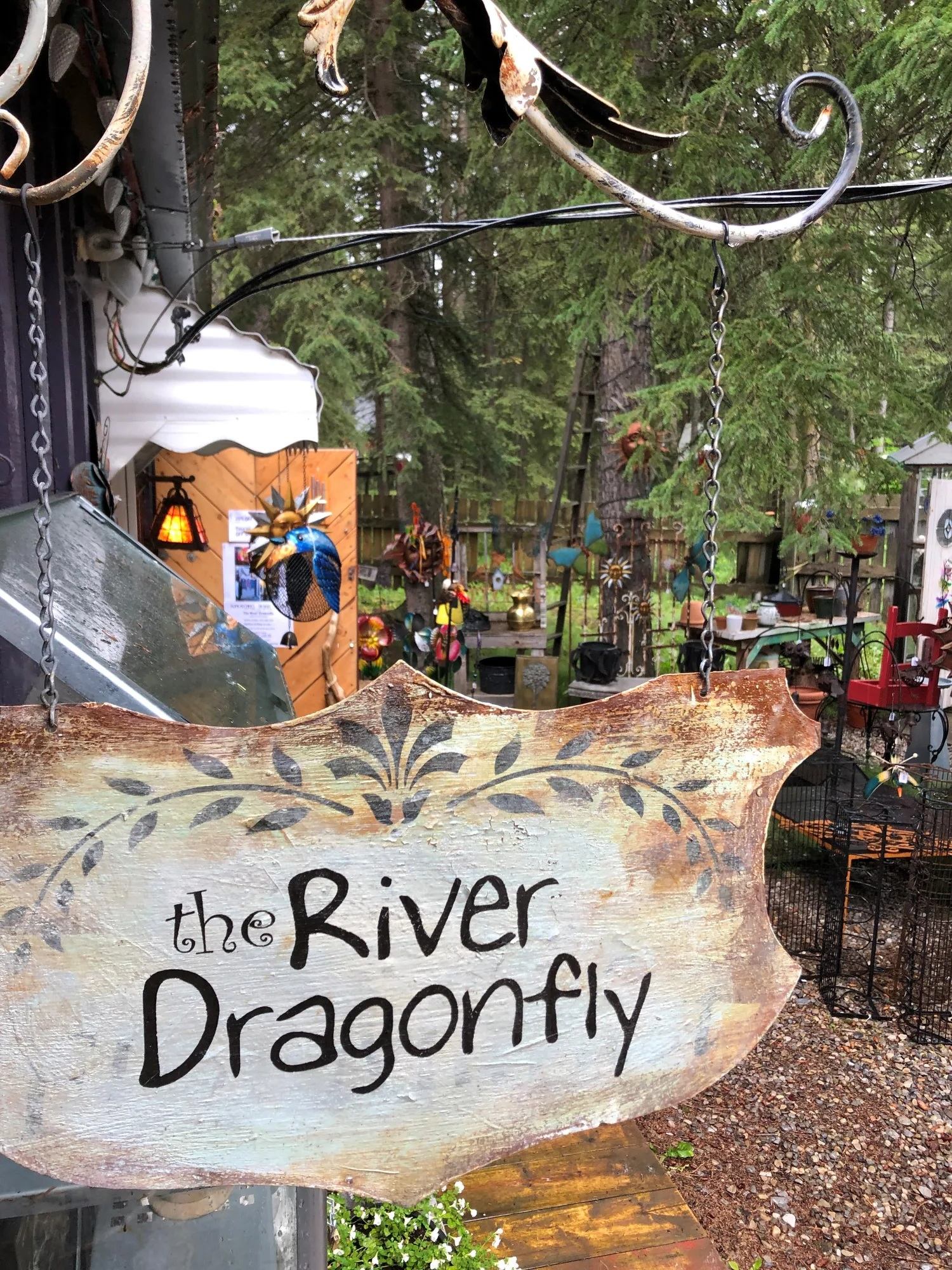 Wooden sign reading “The River Dragonfly” hanging outside a garden art shop.