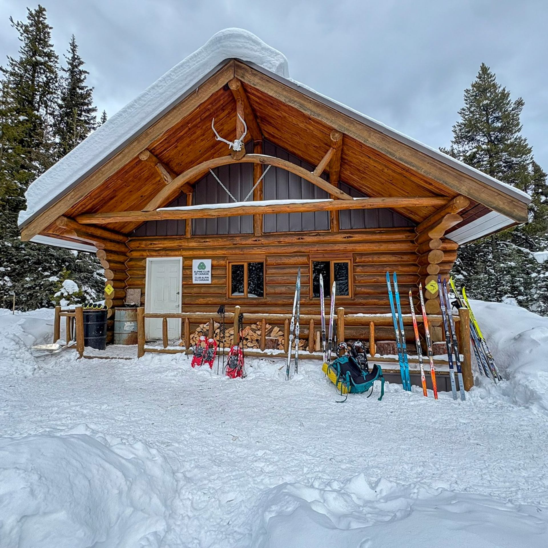 Rustic log cabin in winter with skis and gear standing outside in the snow.