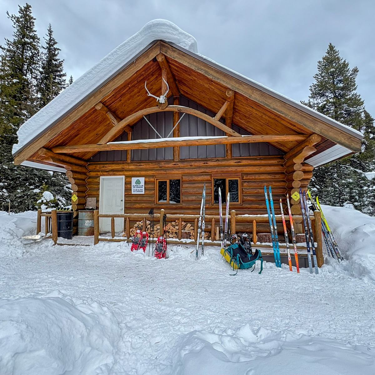 Rustic log cabin in winter with skis and gear standing outside in the snow.