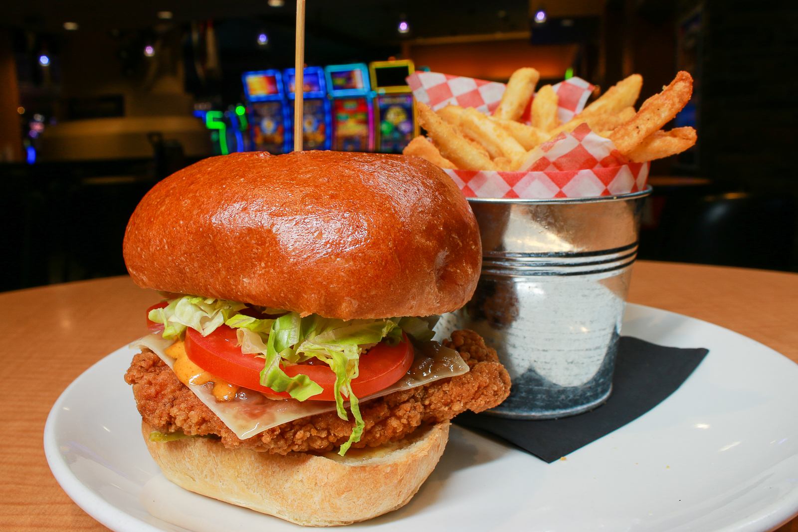 Fried chicken sandwich with fries in a lively lounge setting.