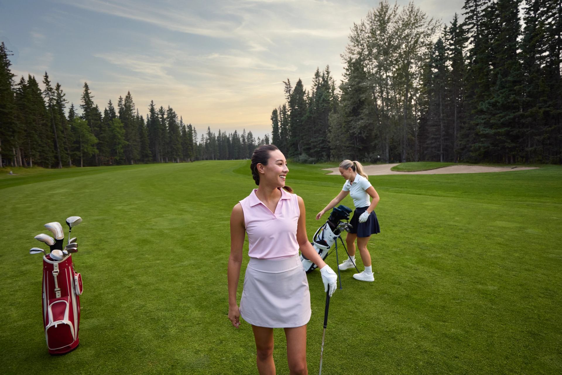 Golfers stand with clubs and bags on a tree-lined fairway.
