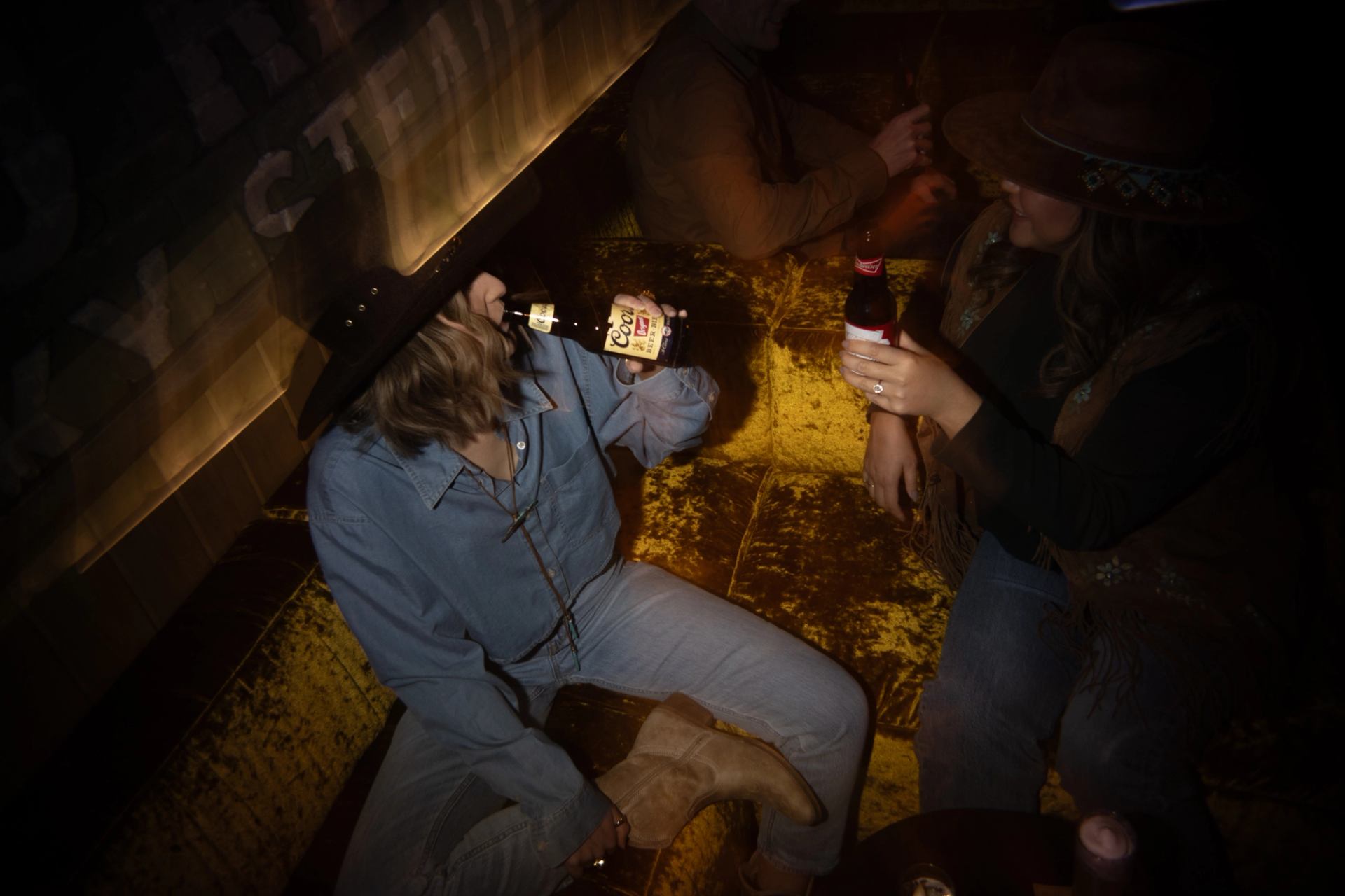 Two people in cowboy hats enjoying drinks together in a dimly lit saloon.
