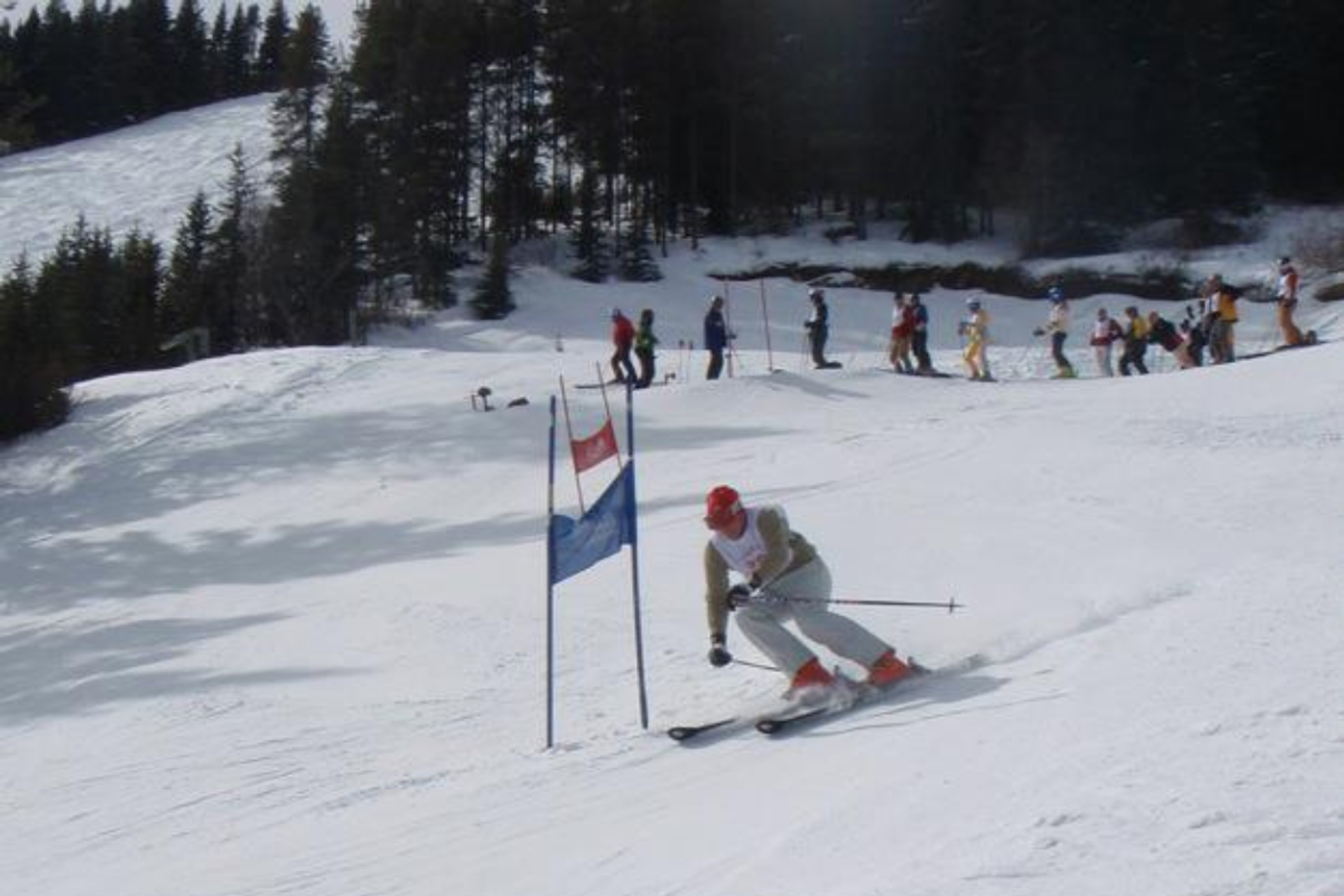 Skier in white outfit carves around a blue gate on a snowy race course.