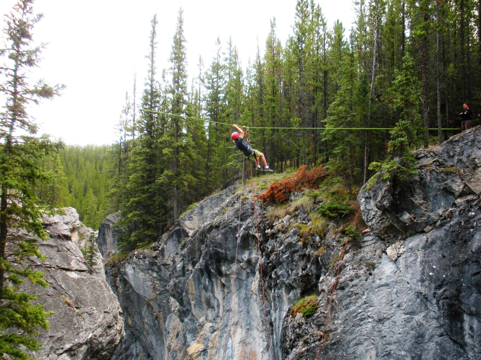 Person standing on rocky cliff surrounded by forest near Frontier Lodge.