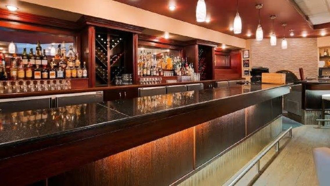 Hotel lounge bar with bottles on shelves, glassware, and dark wooden counter.