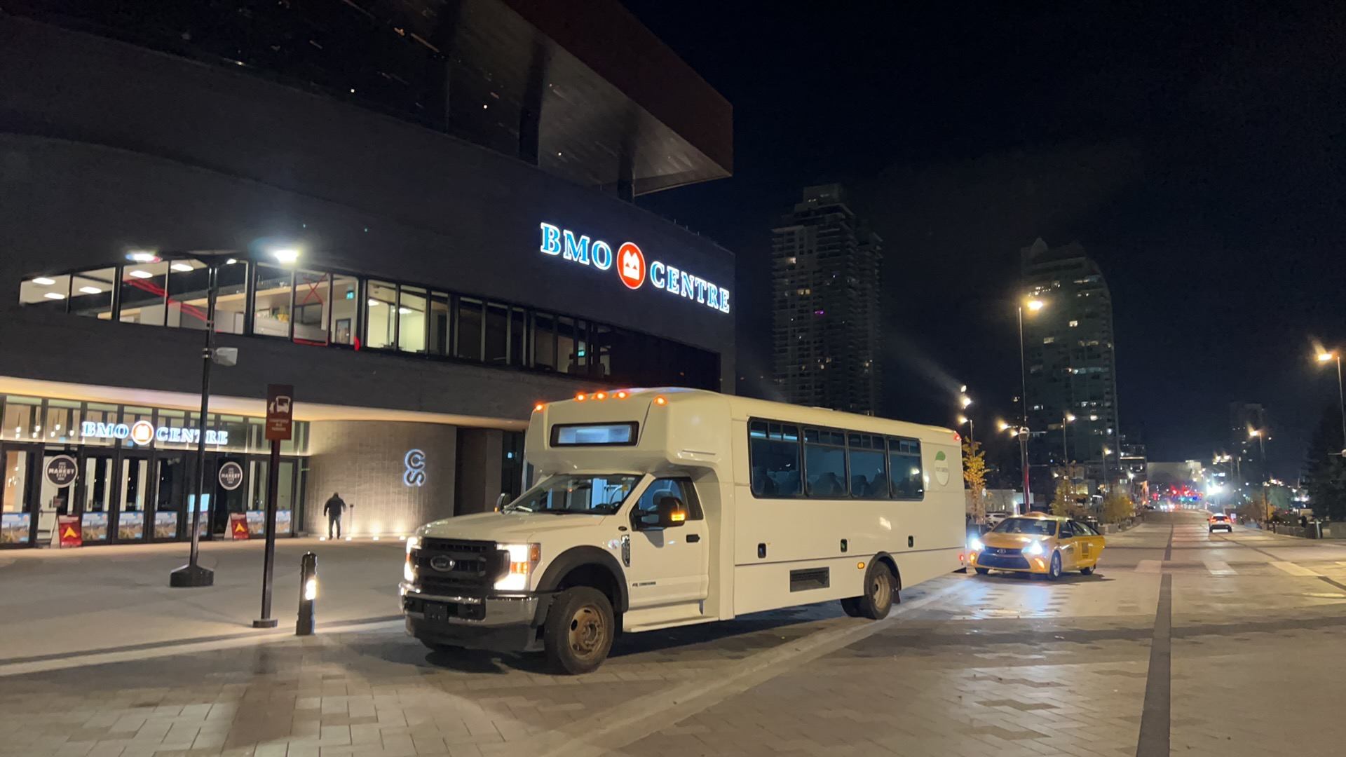 White shuttle bus parked outside BMO Centre on a lit city street at night.