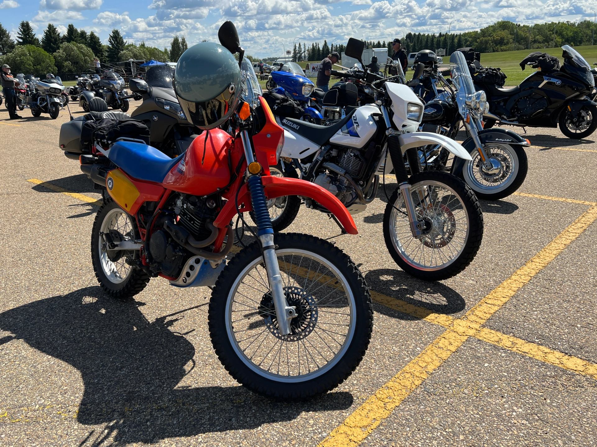 Several dual‑sport motorcycles parked in a sunny lot with blue sky overhead.