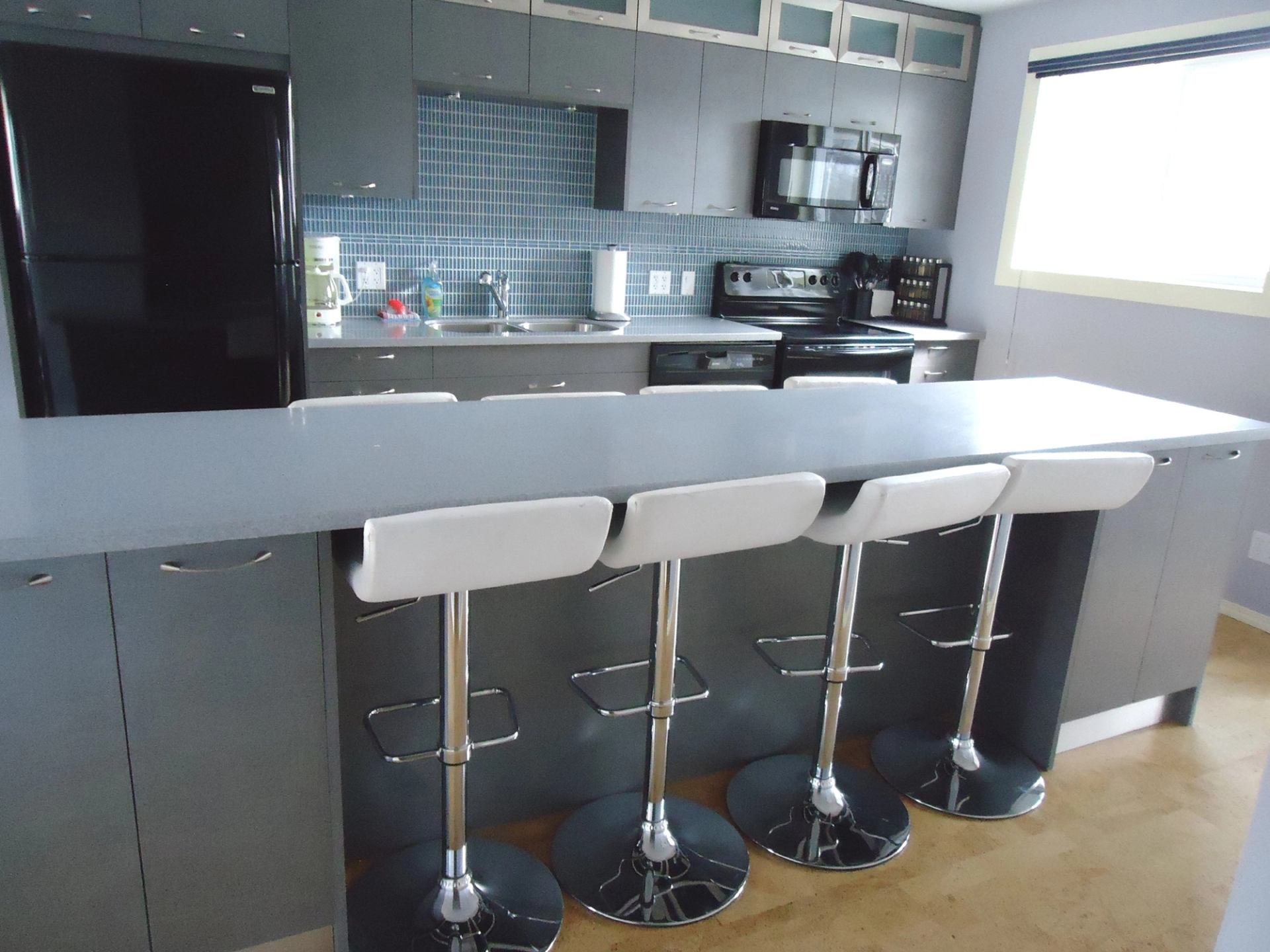 Modern kitchen with grey cabinets, island counter, bar stools, and black appliances.
