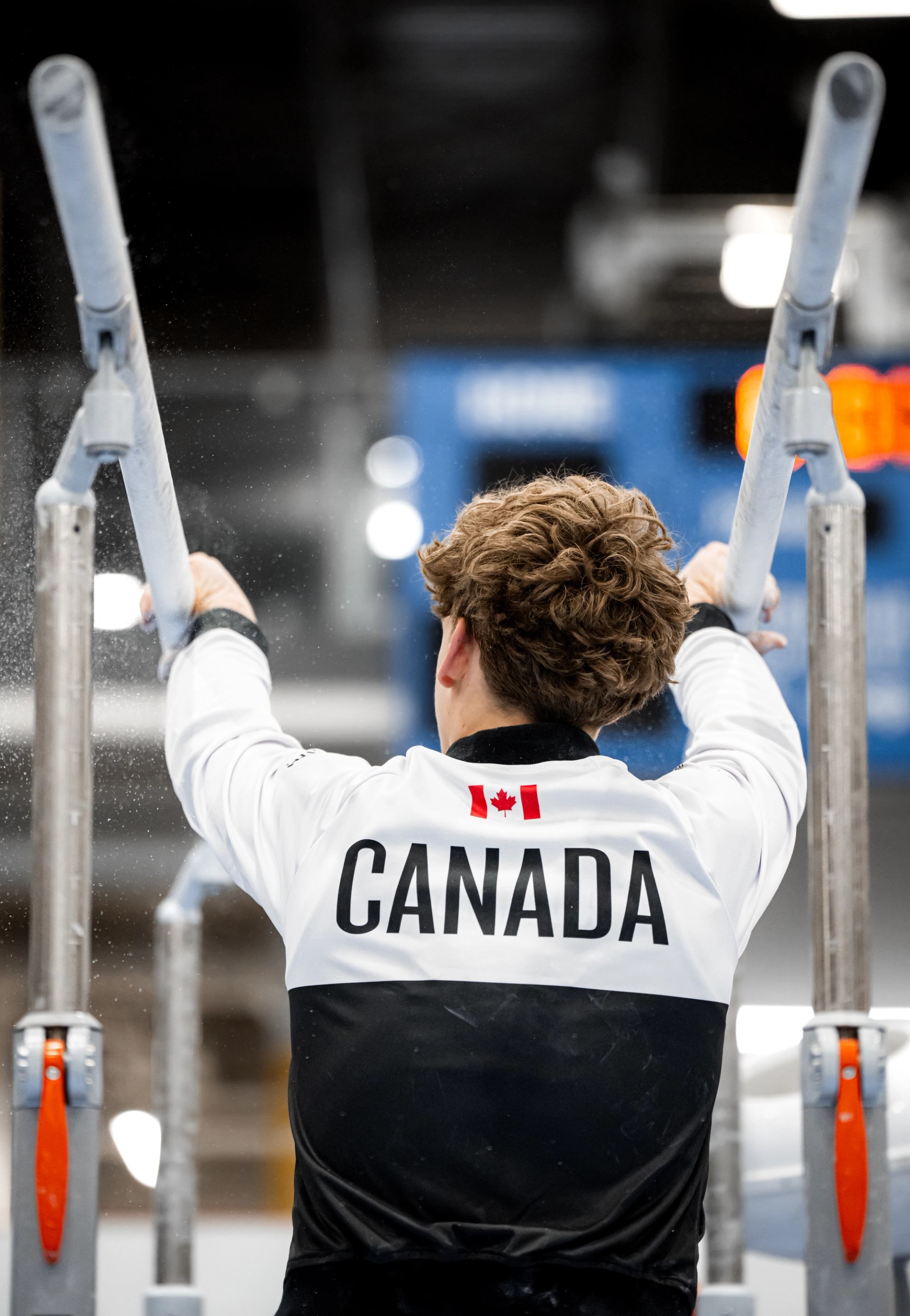 Athlete in a Canada jacket gripping parallel bars before a routine.