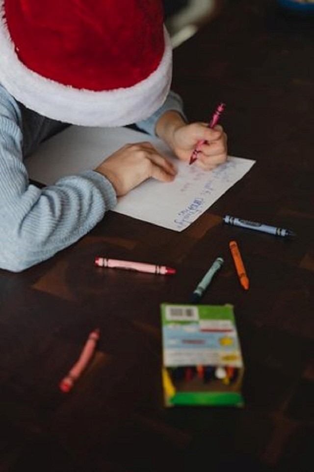 A child in a Santa hat writes a letter to Santa.
