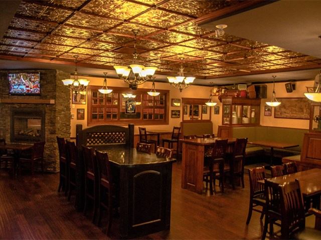 Warm, inviting pub interior with wooden tables, cushioned seating, and ornate ceiling.