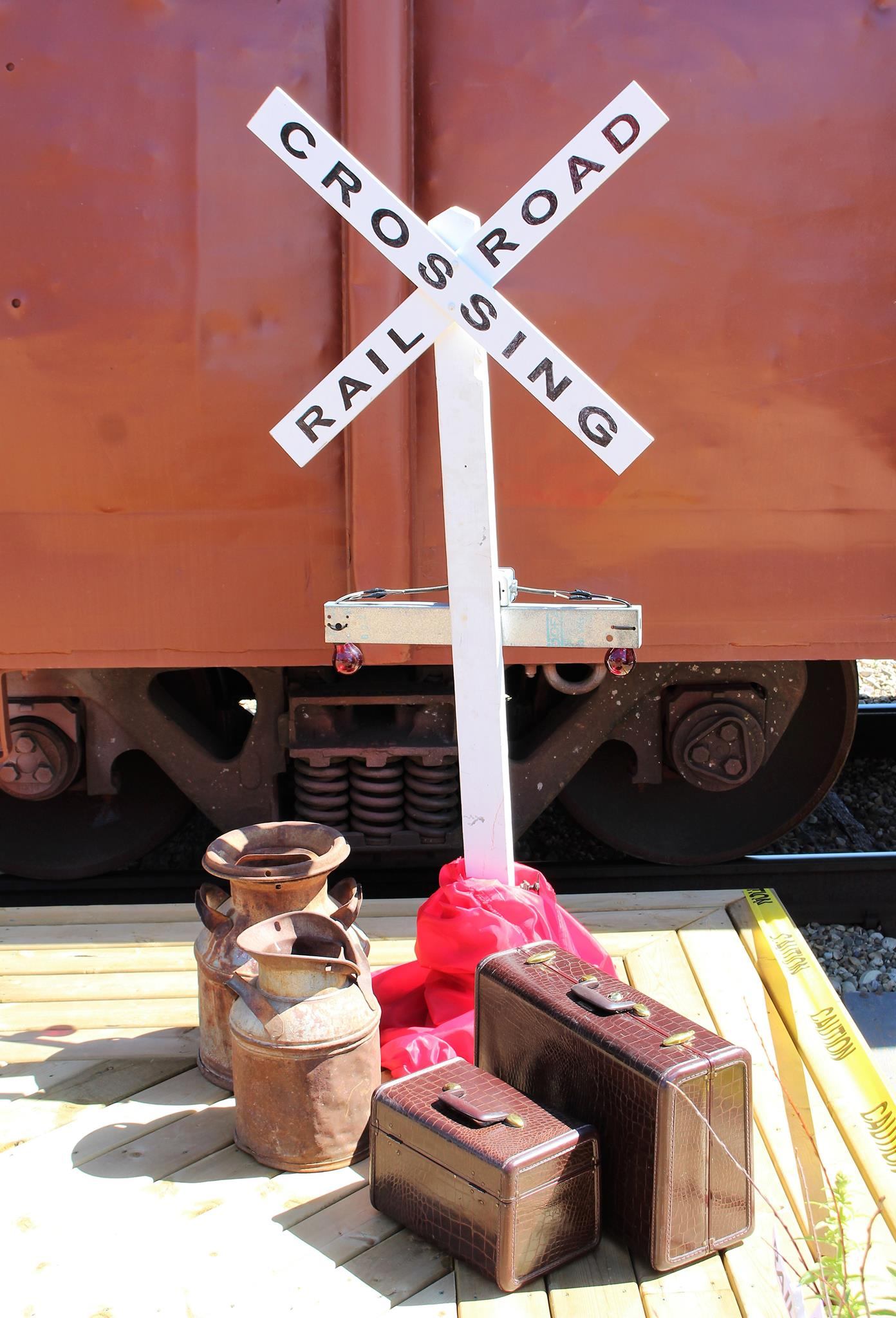Rail crossing sign with antique luggage and metal milk cans on a wooden platform.