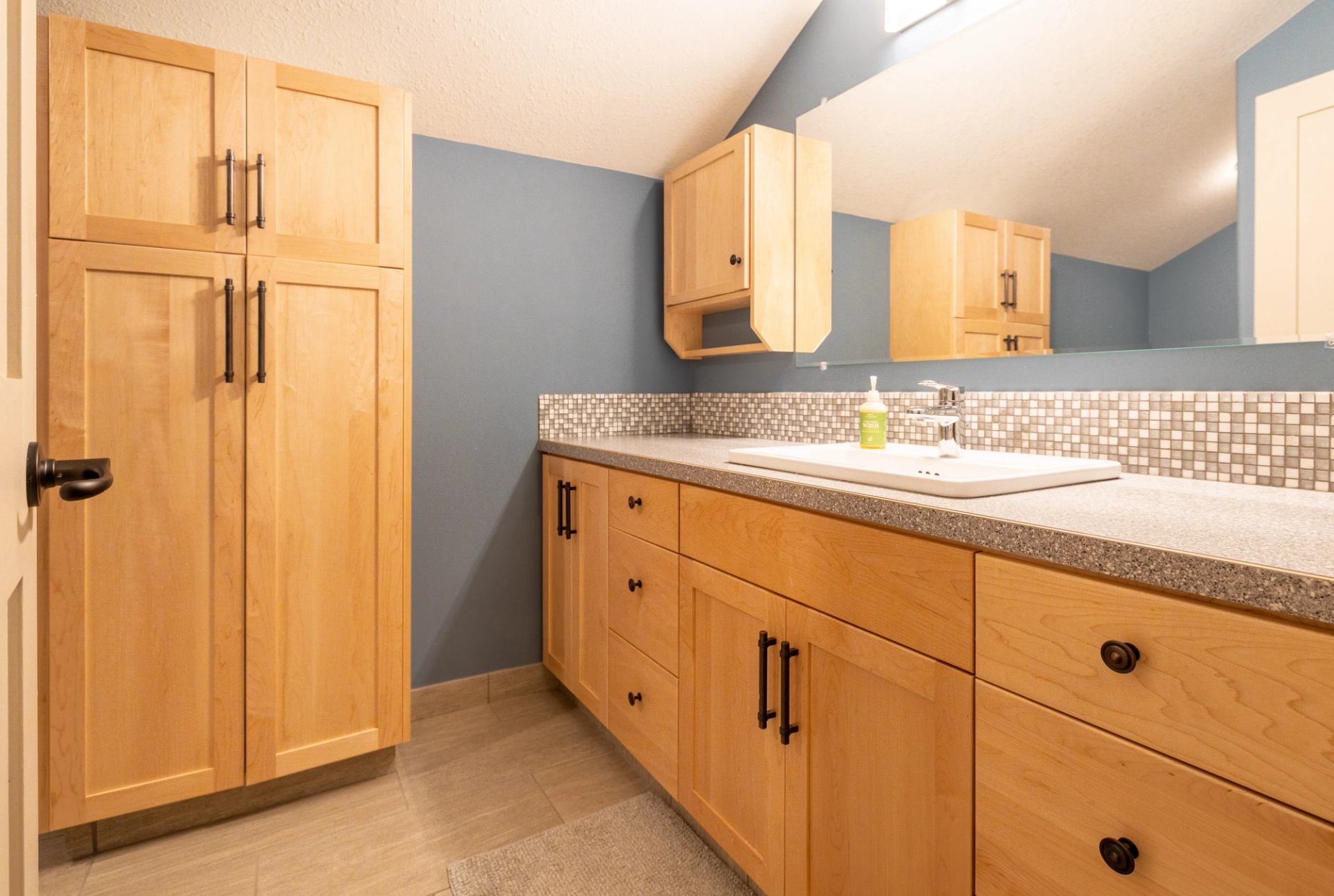 Bathroom with wood vanity, blue walls, and tiled backsplash.