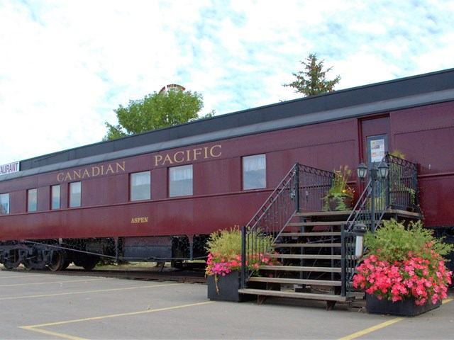 Vintage maroon Canadian Pacific railcar converted into a restaurant with stairs and flowers.