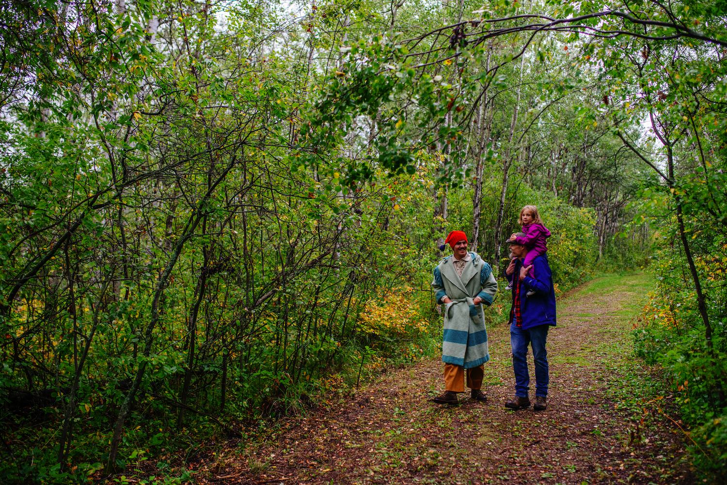 Hikers walk along a wooded path with trees and autumn leaves in the background.