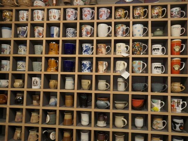 Wooden shelf with assorted mugs in colorful and artistic designs.
