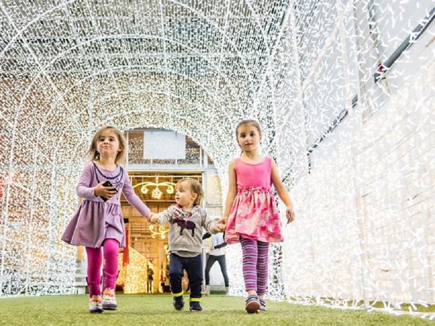 Children walking through a tunnel of glowing holiday lights at Glow Christmas Festival.