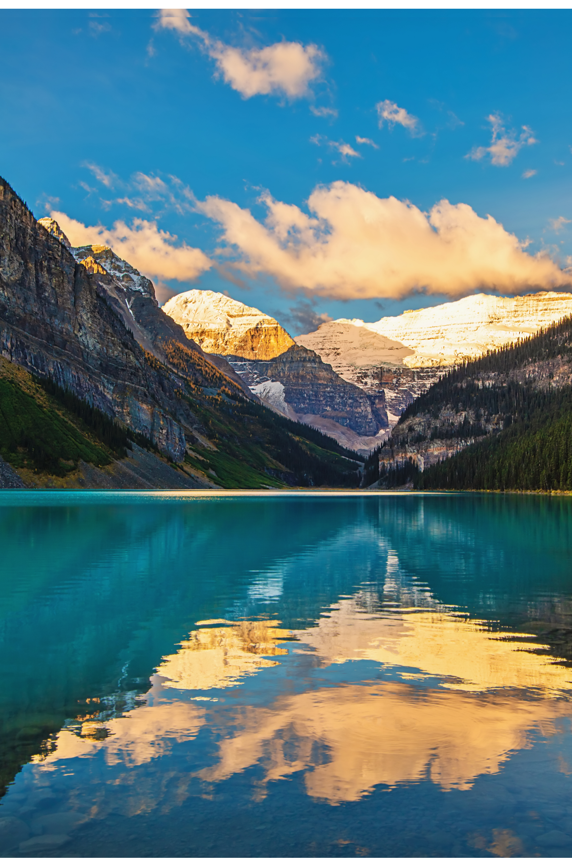 Turquoise lake reflecting sunlit peaks and clouds between steep mountain walls.