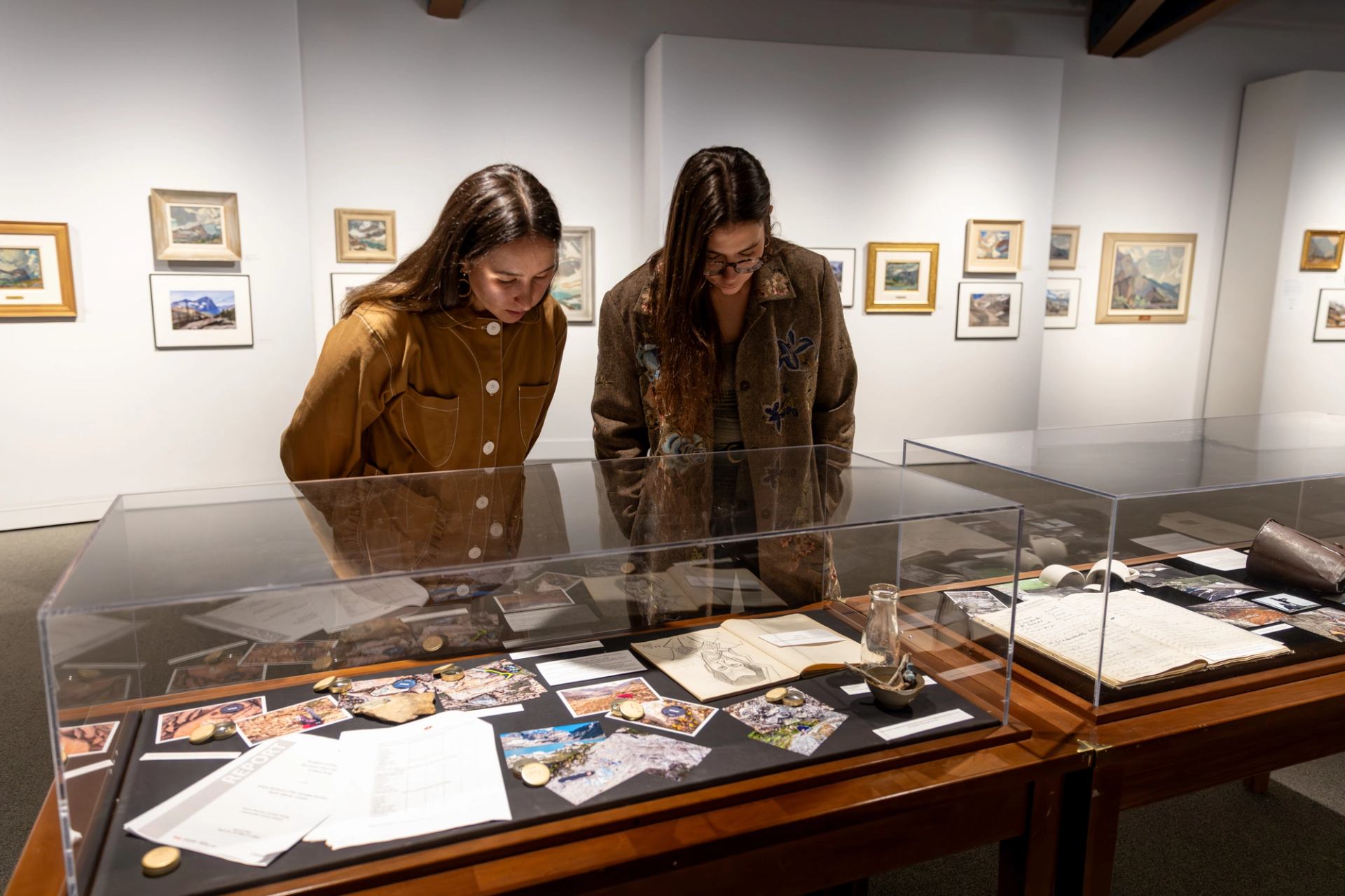 Two visitors look into a glass case of photographs, notes, and artifacts.