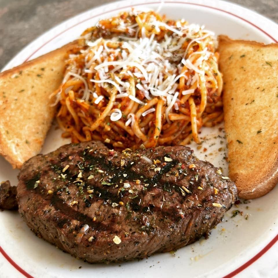 Plate with seasoned steak, spaghetti topped with cheese, and two slices of garlic bread