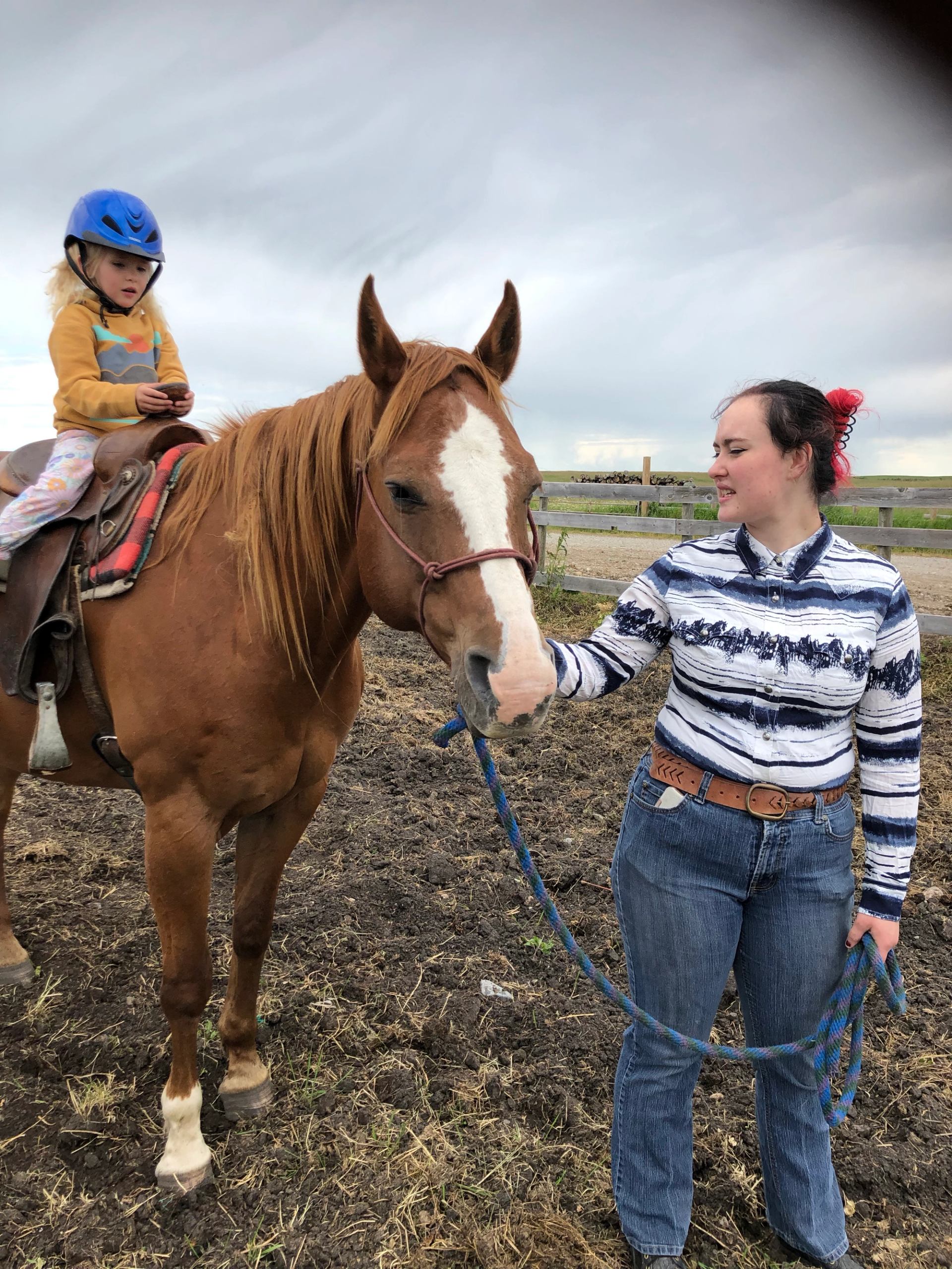 A person holding a horse’s lead while a child sits on the saddled horse.