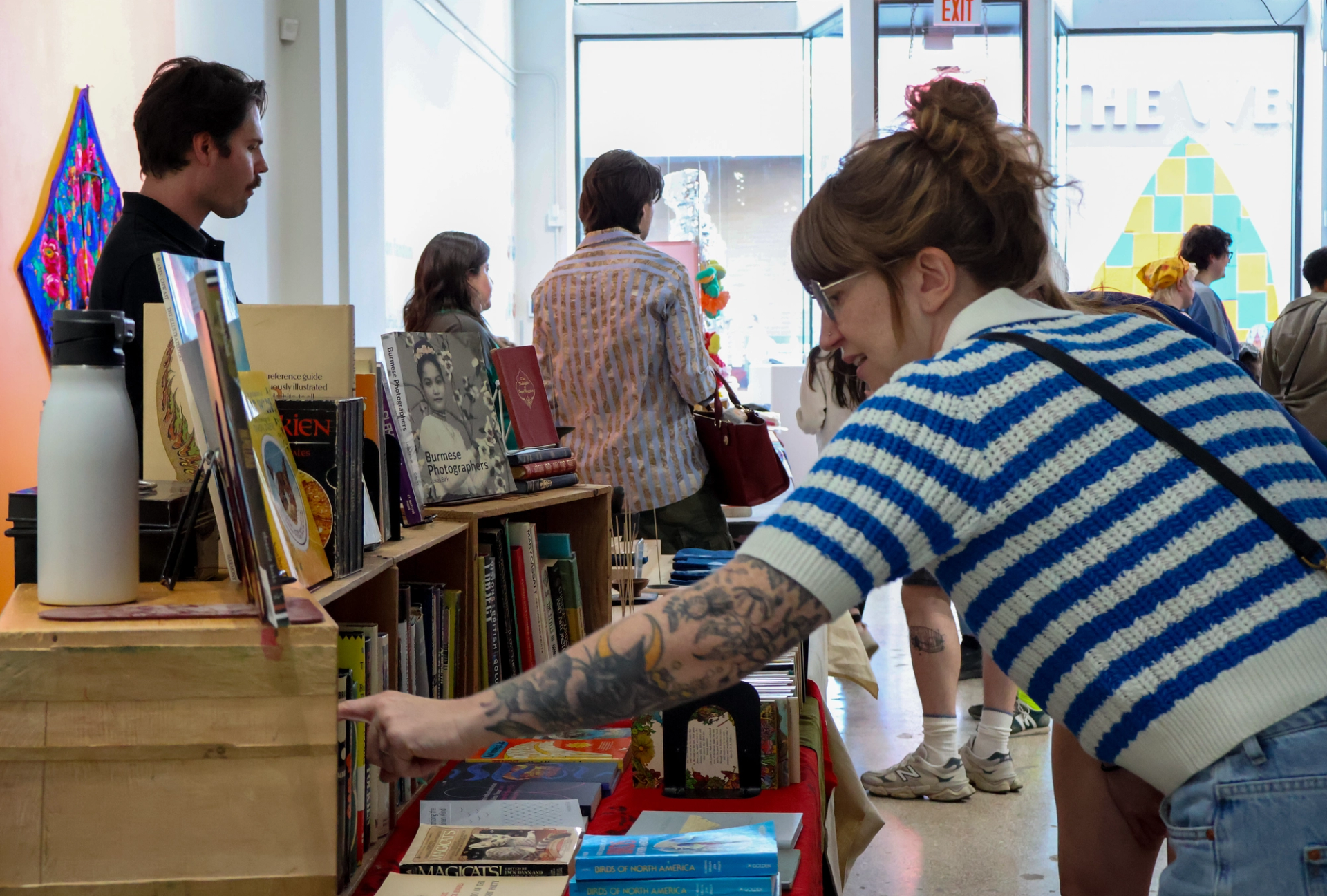 Woman reaches for book from a stand in the gallery, brightly lit, daytime.