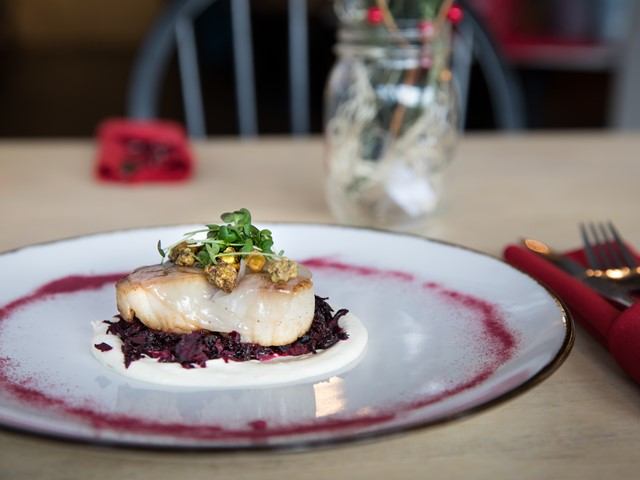 Plated fish fillet on puree with shredded beets and microgreens in restaurant setting.