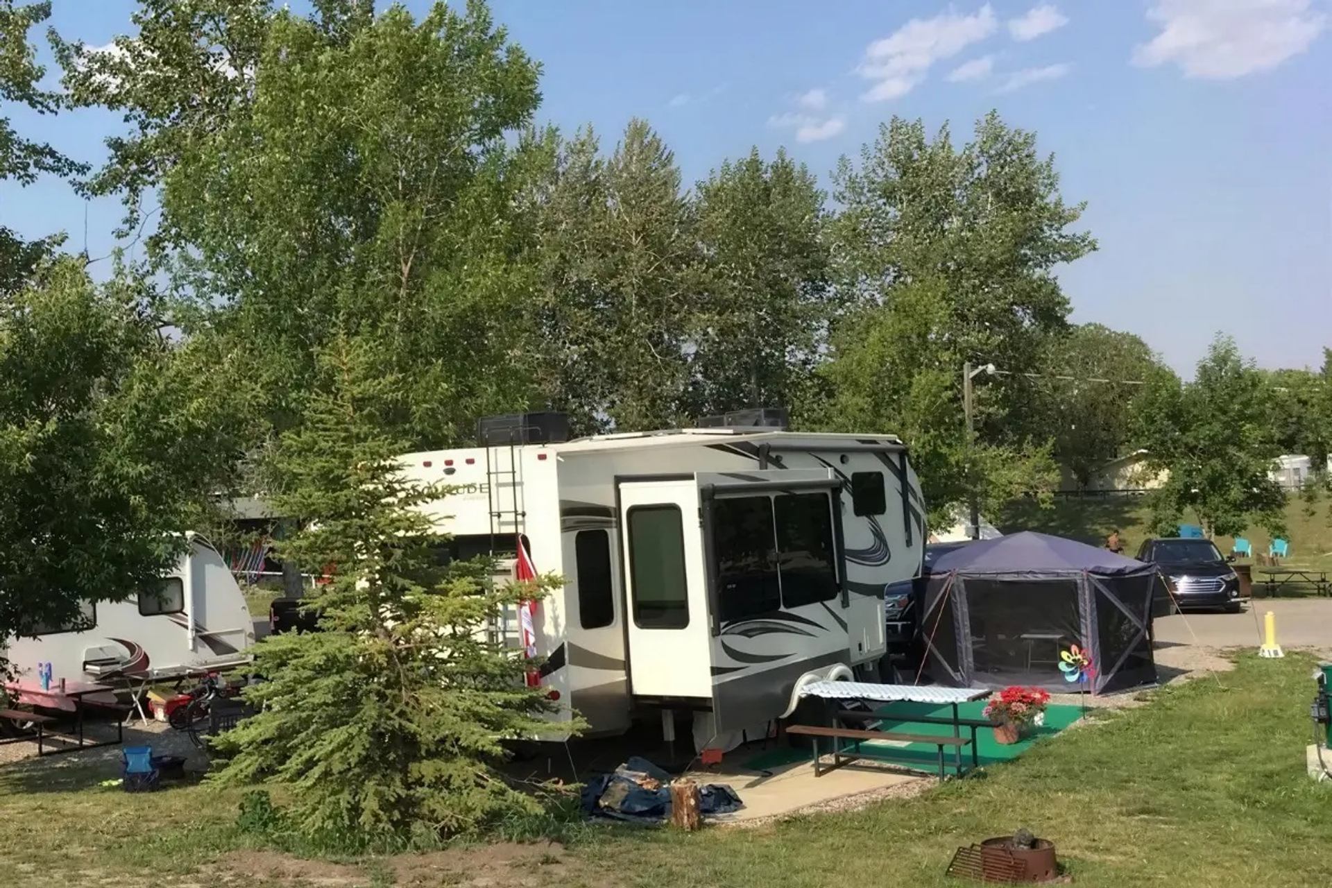 Campsite with large RV, picnic table, screen tent and trees in the background.