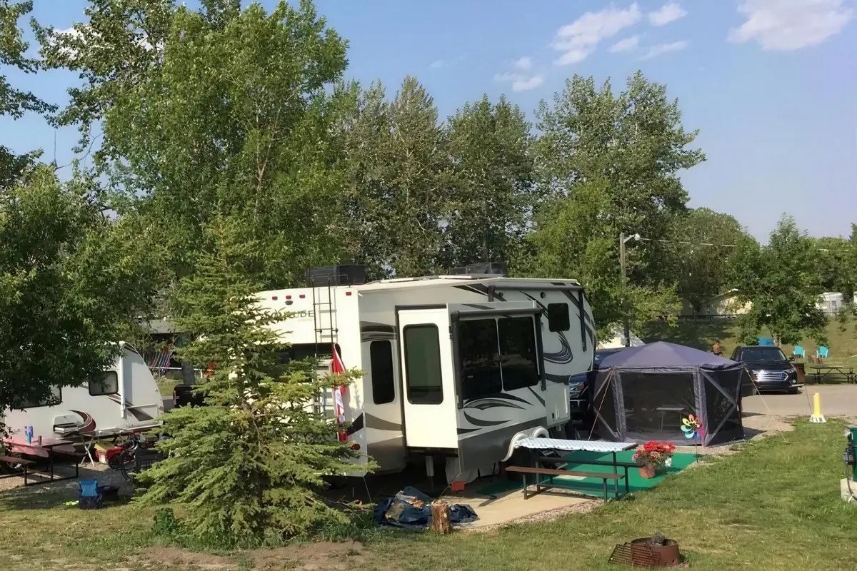 Campsite with large RV, picnic table, screen tent and trees in the background.