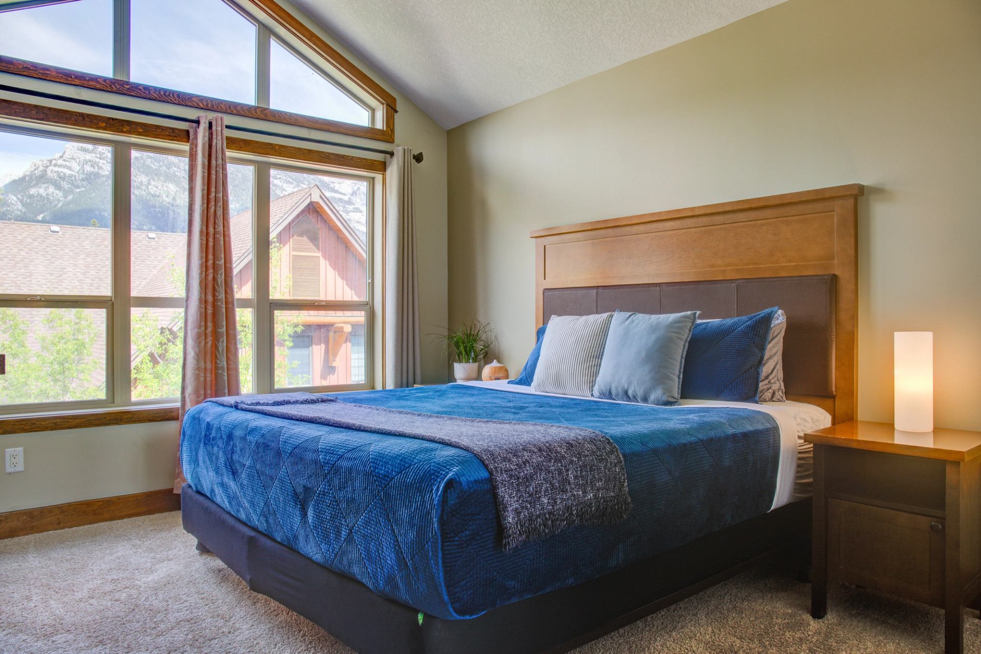 Bright bedroom with large windows, mountain views, and a cozy blue bedspread.