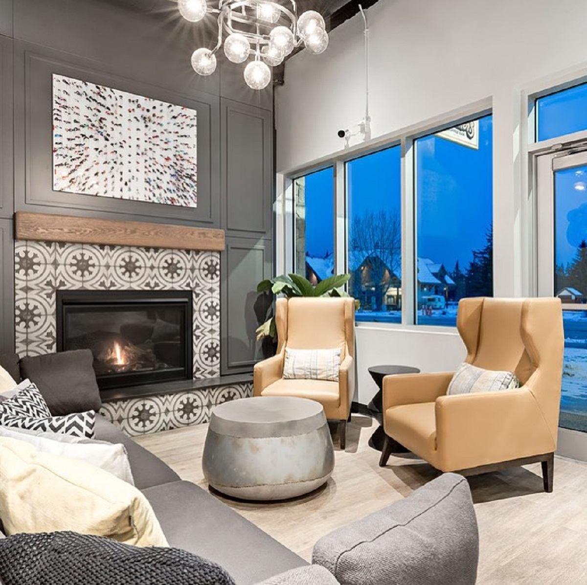 Modern lounge with fireplace, tan armchairs, round table and large windows showing snowy street.