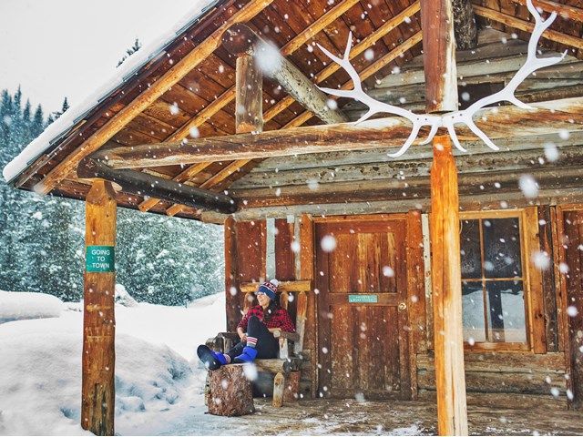 Woman sitting outside a log cabin in the snowy forest at Sundance Lodge in Banff.