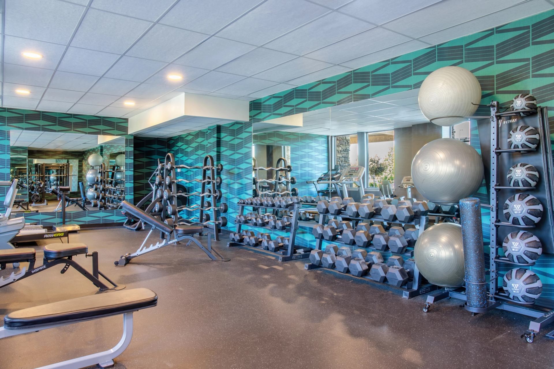 brightly lit gym, featuring free weights, machines and exercise balls. Mirrored walls.