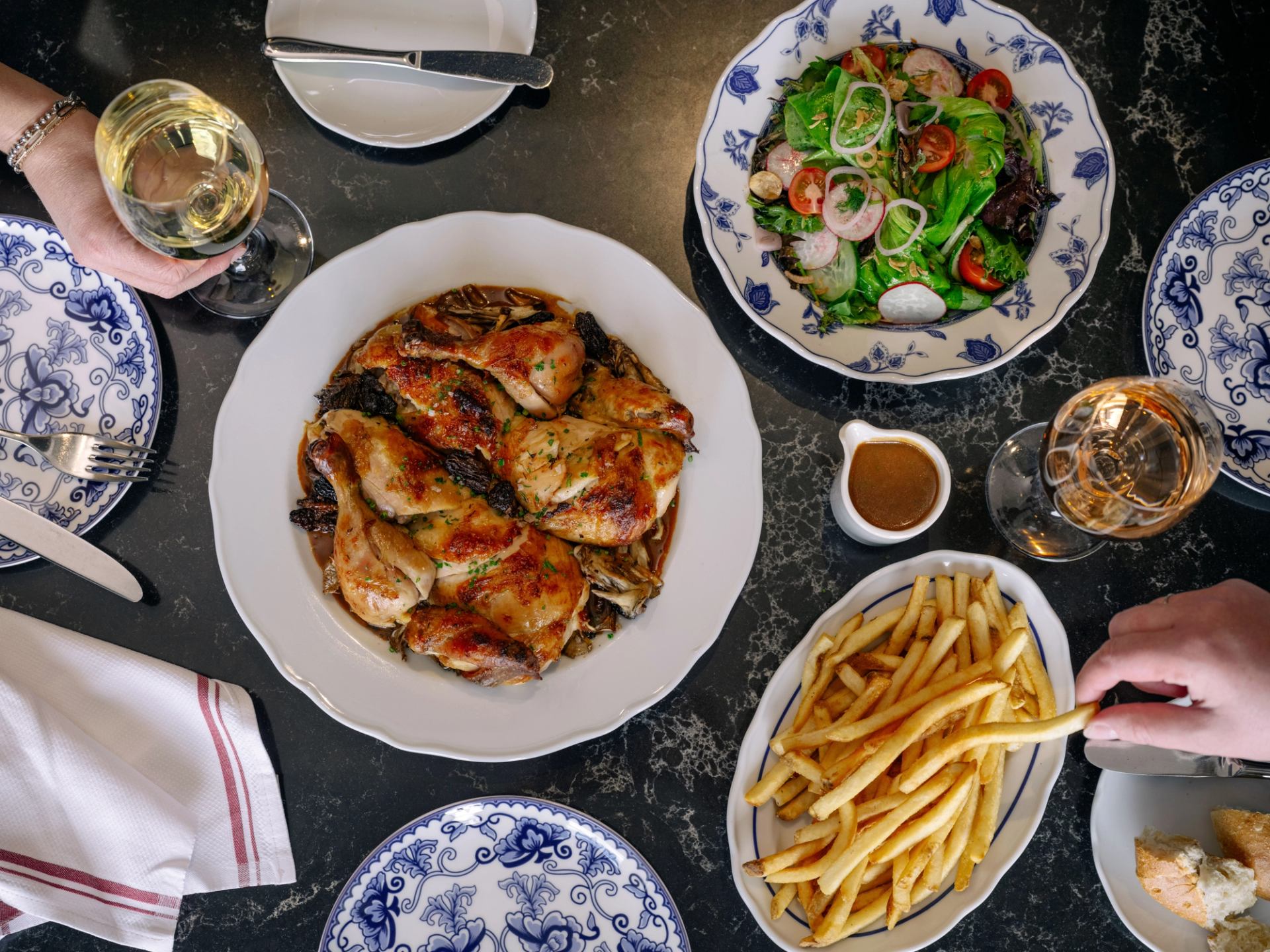 Table with roast chicken, fries, salad, wine glasses, and patterned plates.