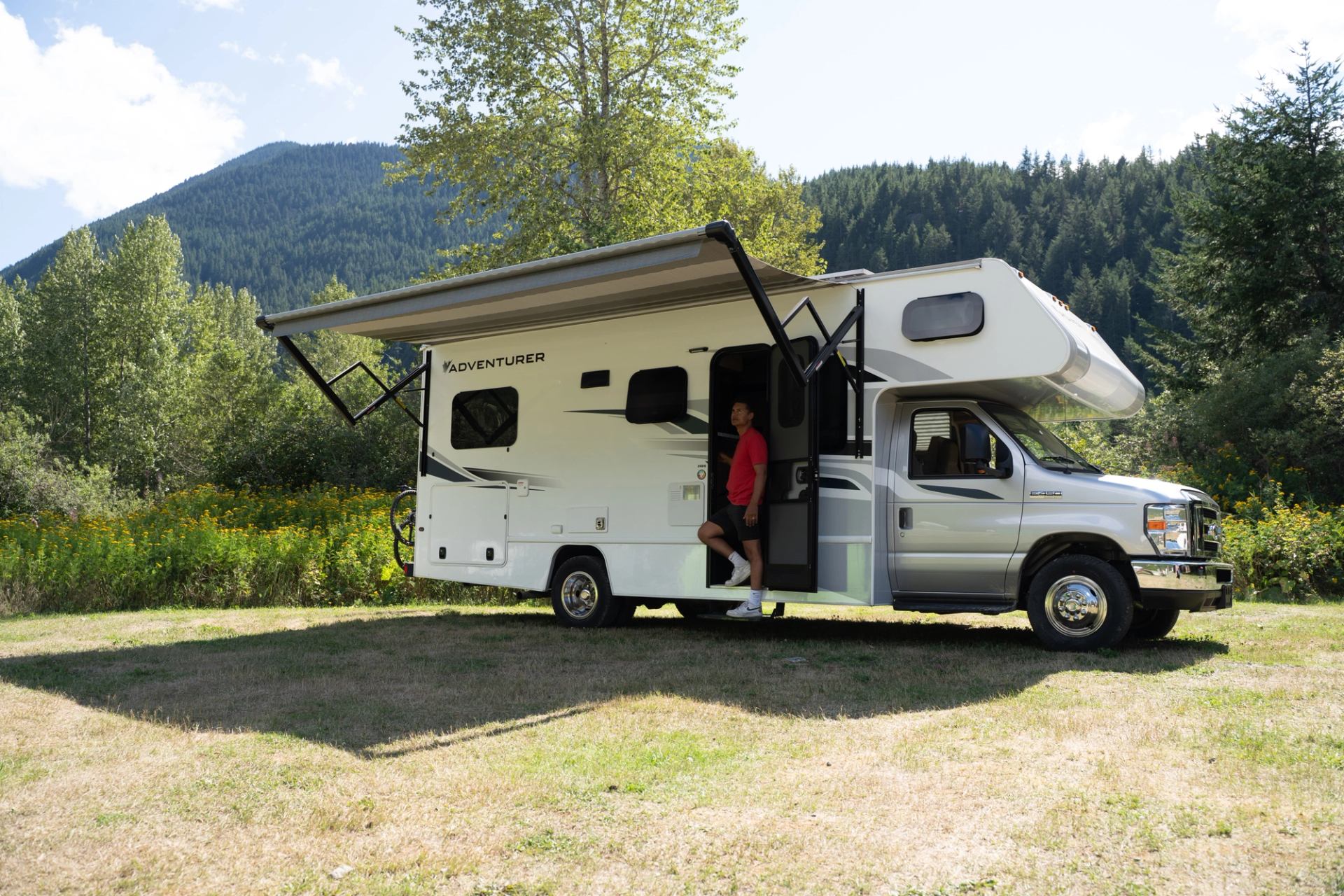 RV with awning parked near trees and mountains.
