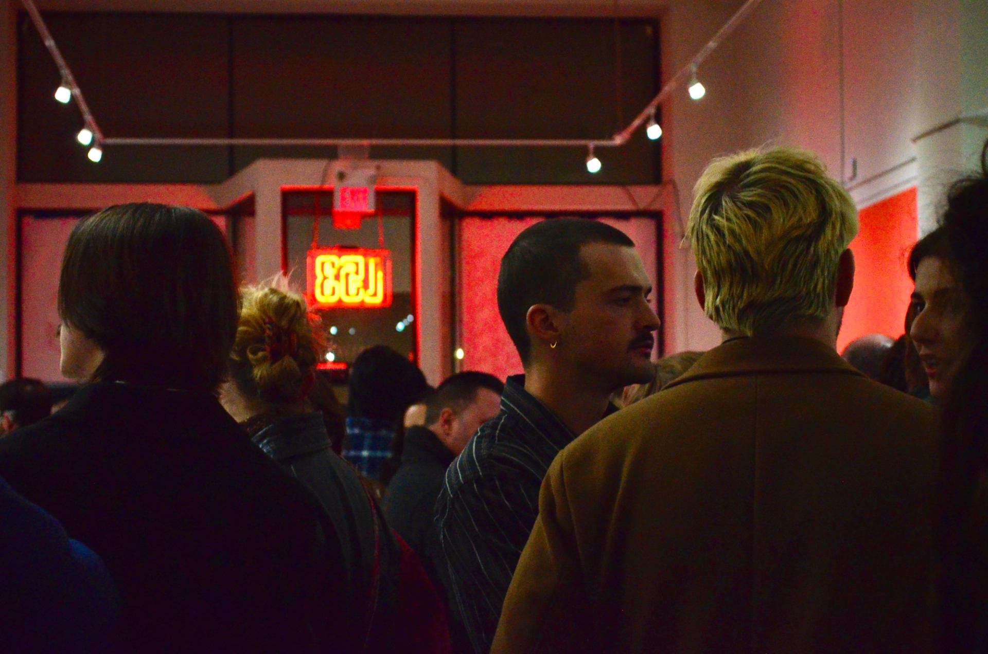 Latitude 53 in the evening, the L53 neon sign glows orange in the window illuminating gallery guests