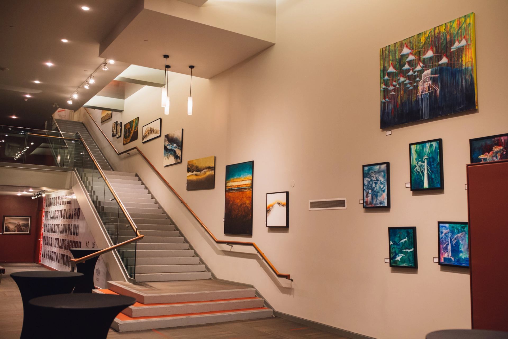Art gallery staircase with colourful abstract paintings on cream walls and modern lighting.