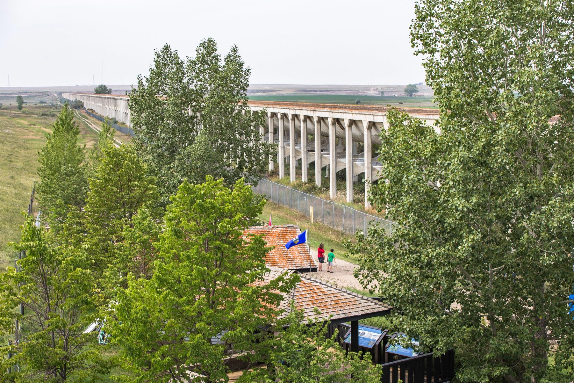 Concrete aqueduct stretches across open landscape above trees and small visitor area below.