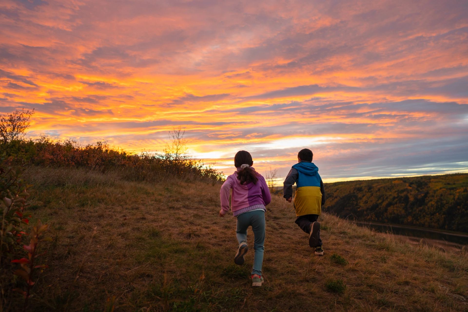 Two kids running on a hill at sunset with vibrant clouds overhead.