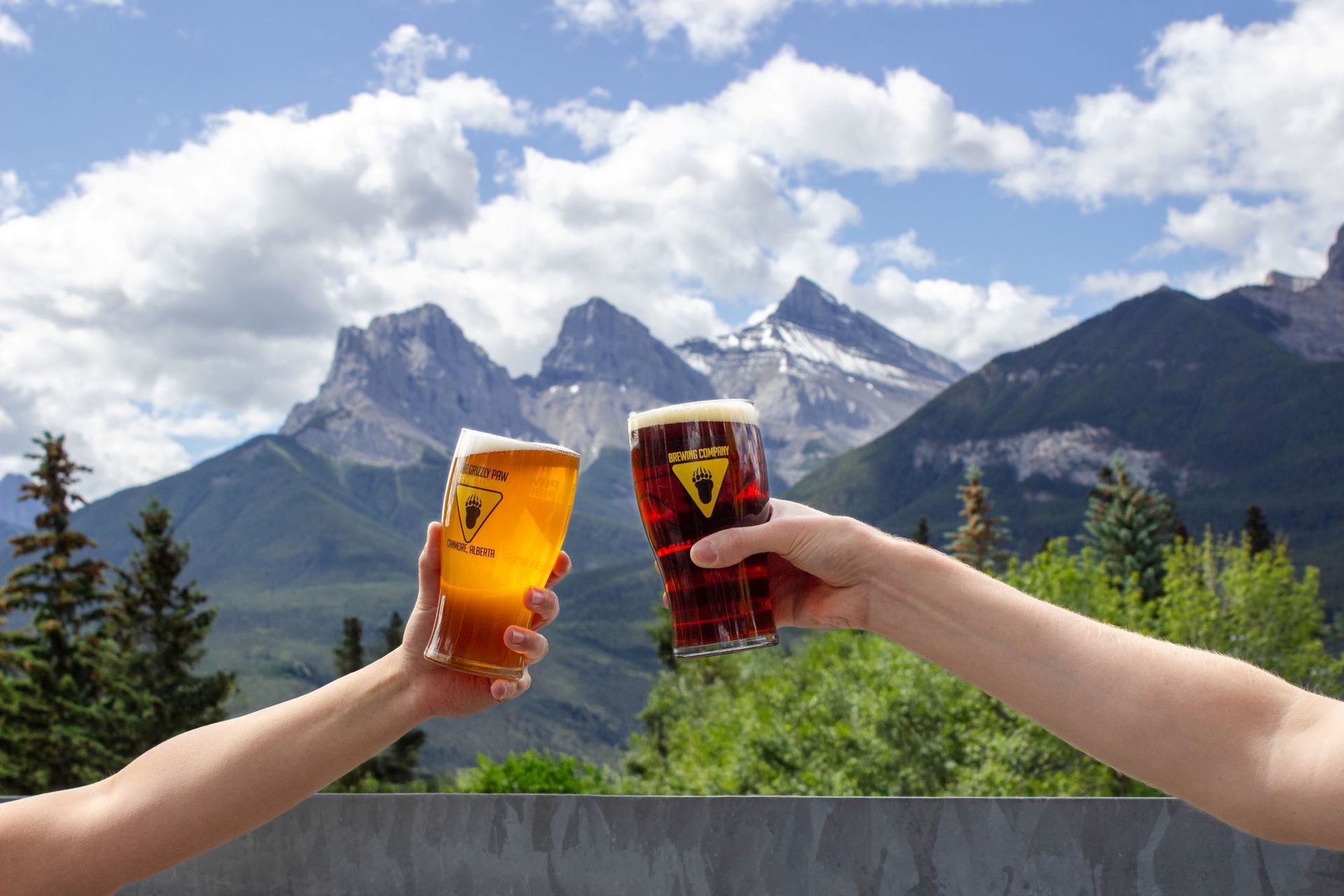 Two glasses of craft beer clinking with mountain peaks in the background at The Grizzly Paw Brewing Company.