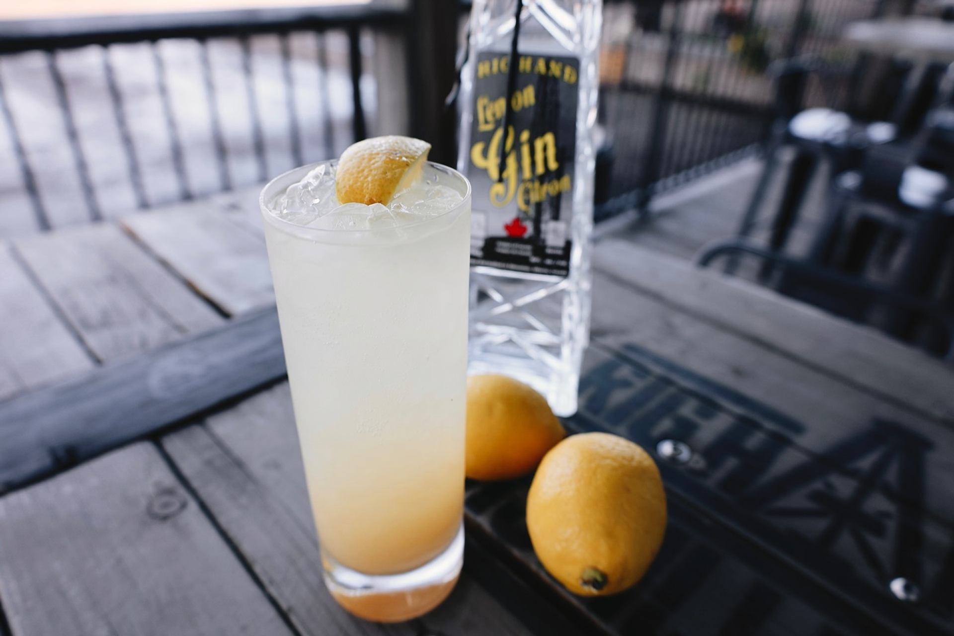 A chilled lemon cocktail sits beside a bottle of gin and fresh lemons on a patio table.