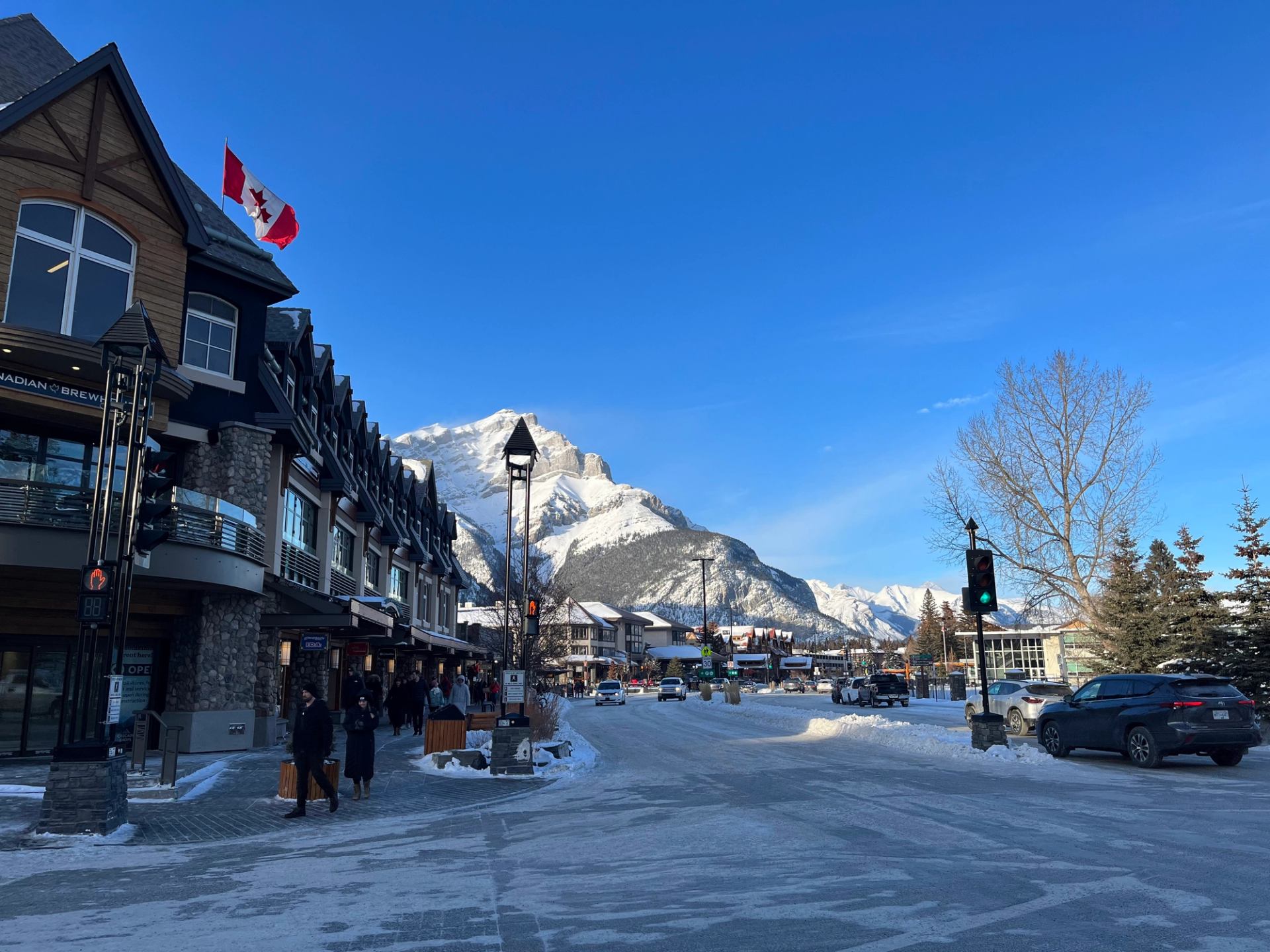 Banff Avenue lined with shops, snow, and mountain views on a clear day.
