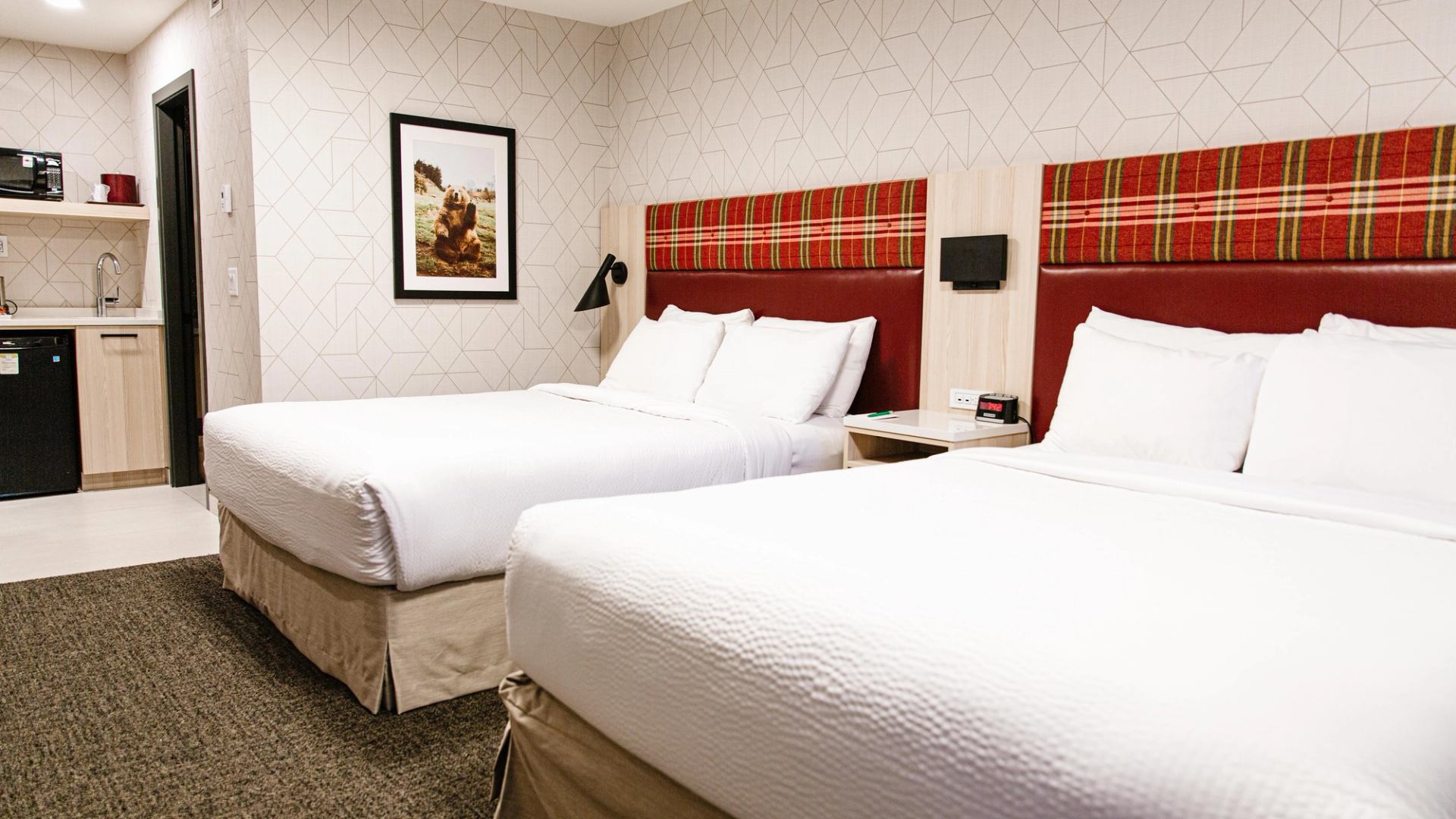 Modern lodge room with two double beds, plaid headboards, and a kitchenette.