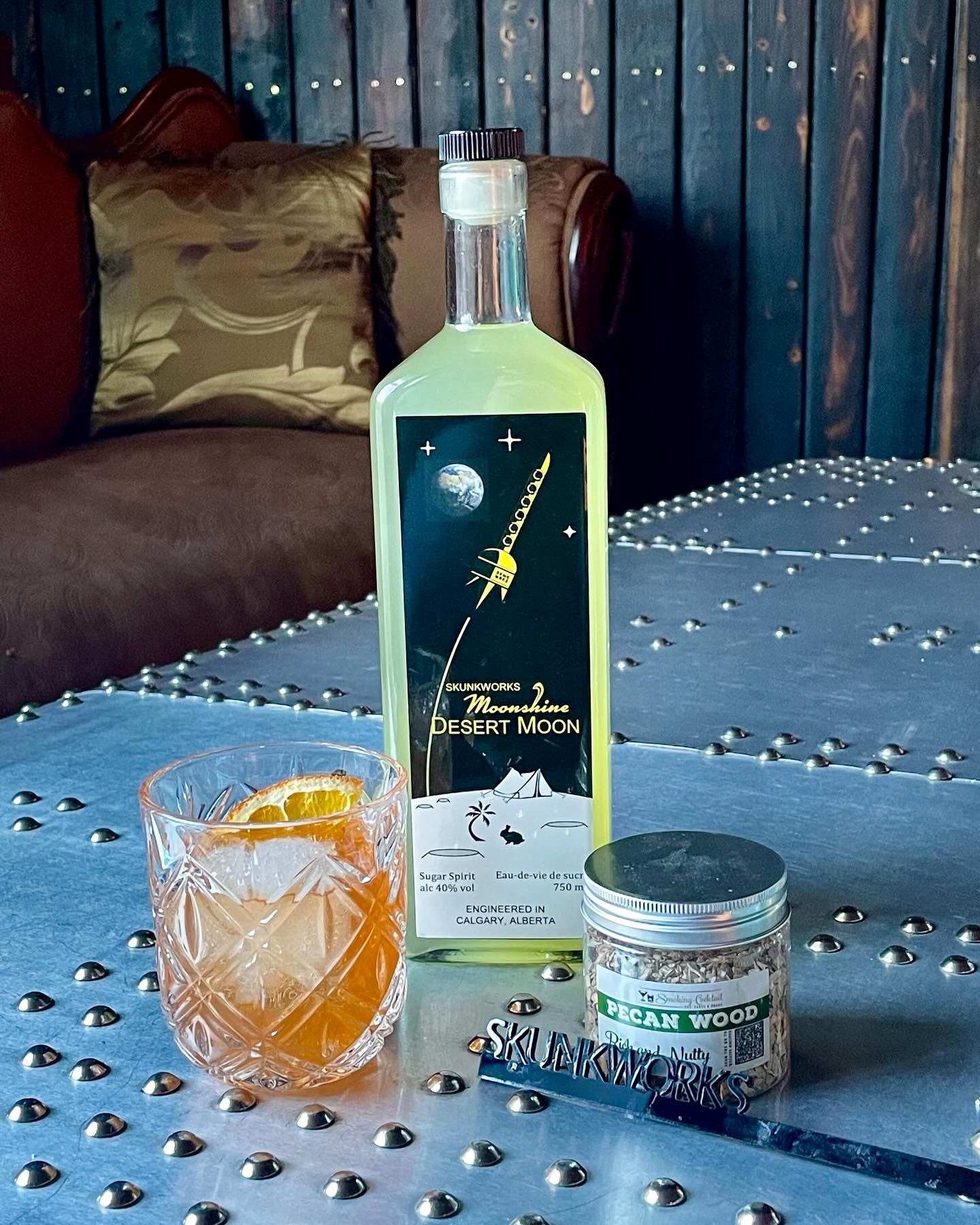 Desert Moon moonshine bottle with a cocktail glass and pecan wood garnish.