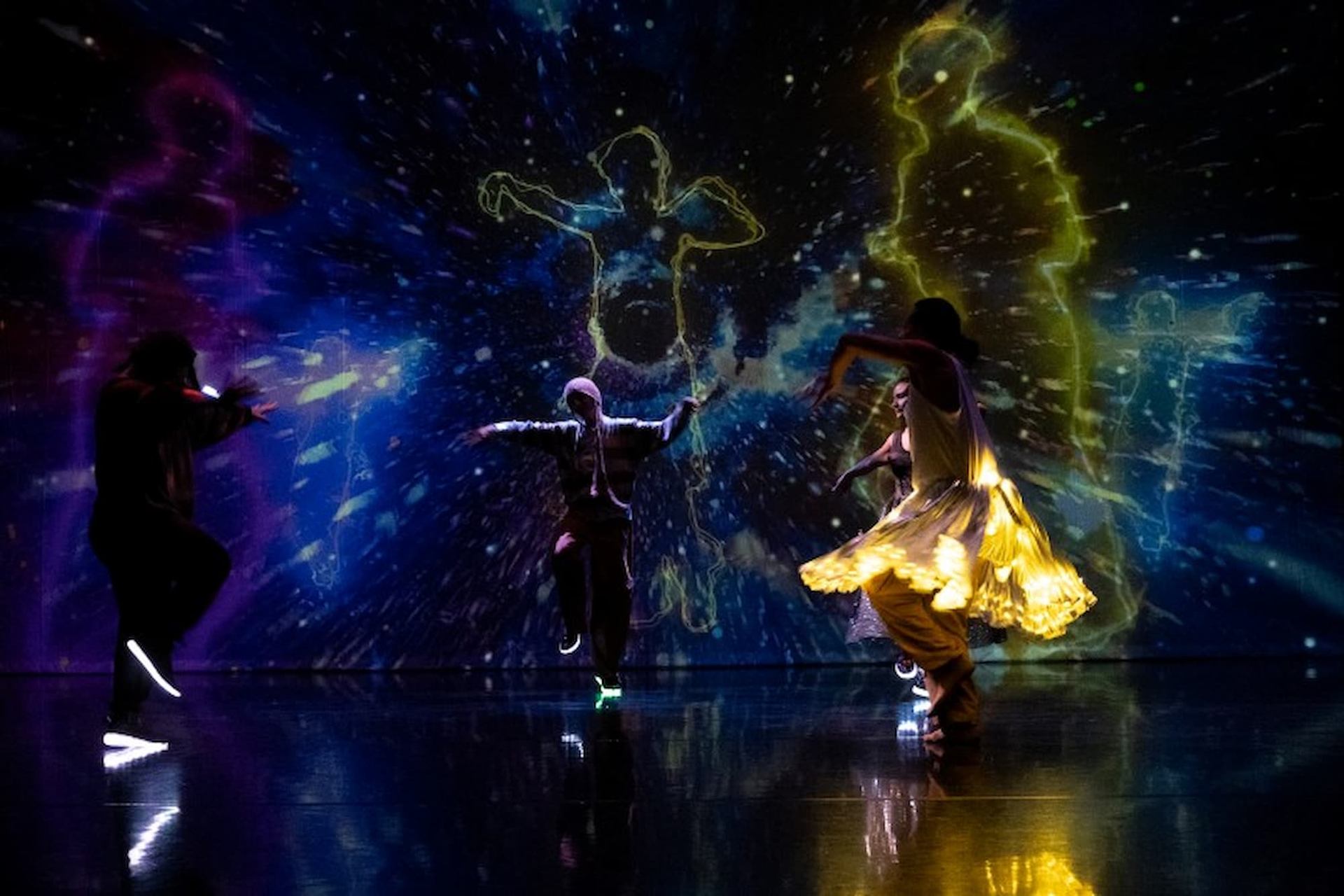 Dancers performing in front of colorful, glowing silhouettes and swirling light effects.