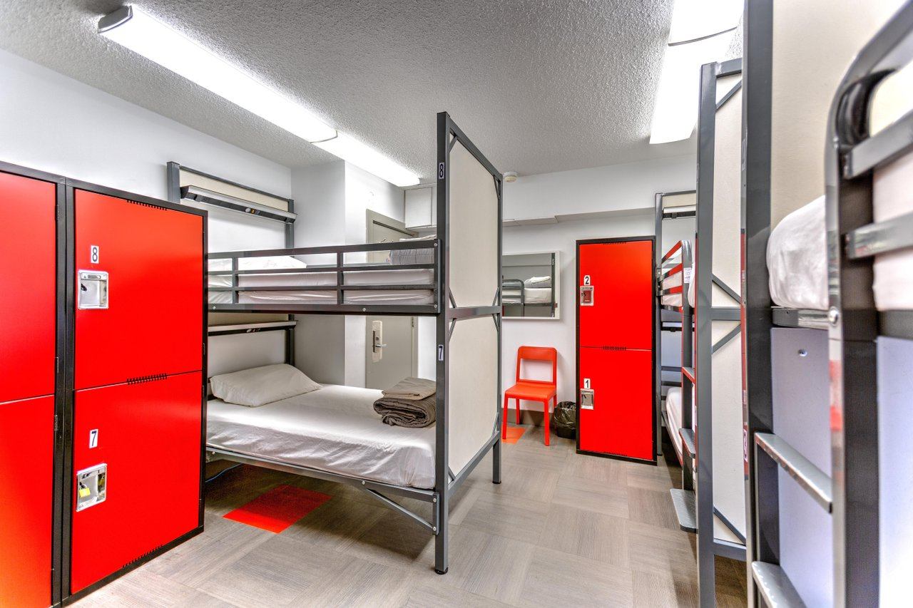 Modern dorm room at with metal bunk beds, bright red lockers, and clean white walls.