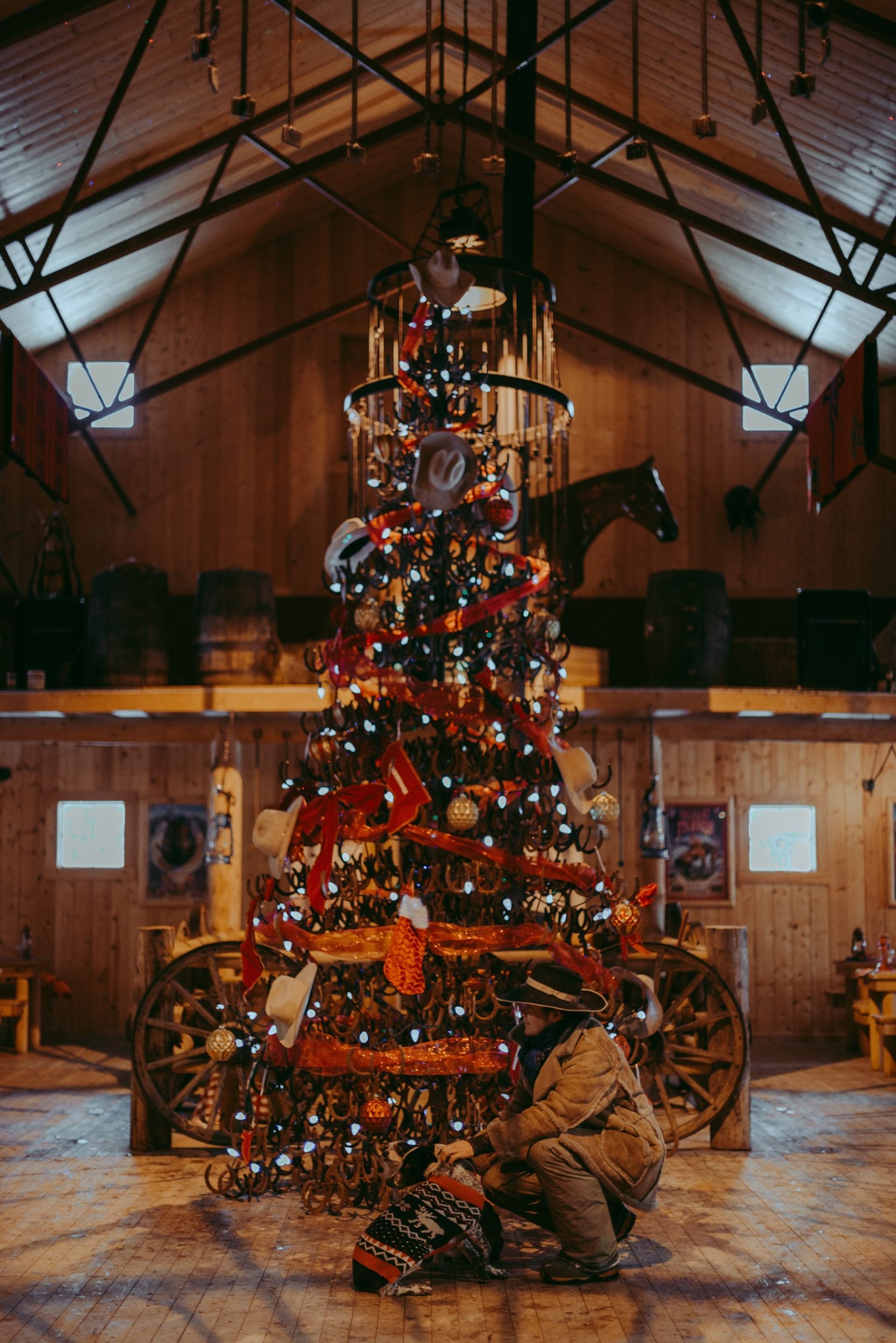 Decorated Christmas tree in rustic barn with two people nearby.