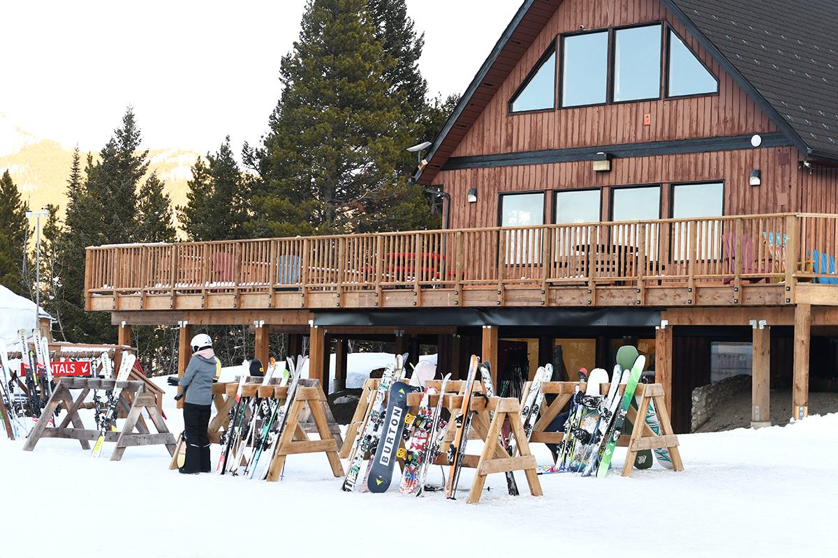 Wooden ski lodge with racks of skis and snow-covered ground at Pass Powderkeg.