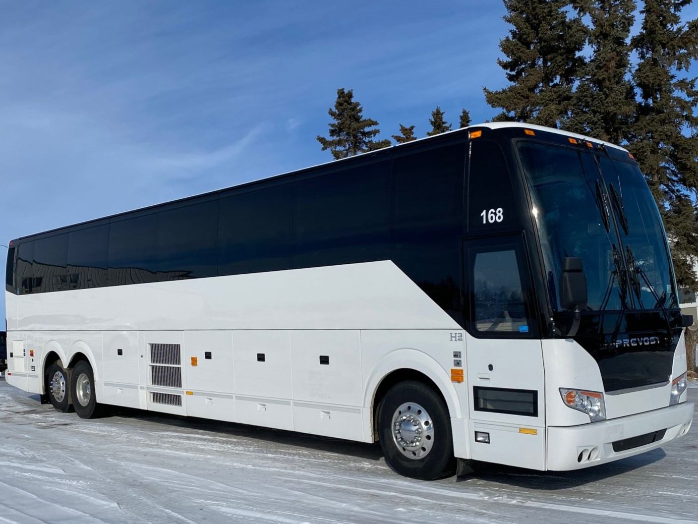 A large white luxury coach bus parked on a snowy road, ready for custom tours through Alberta and BC.