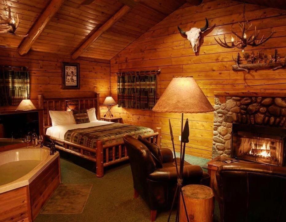 A rustic cabin-style bedroom with wooden beams, stone fireplace, and Western-themed decor.